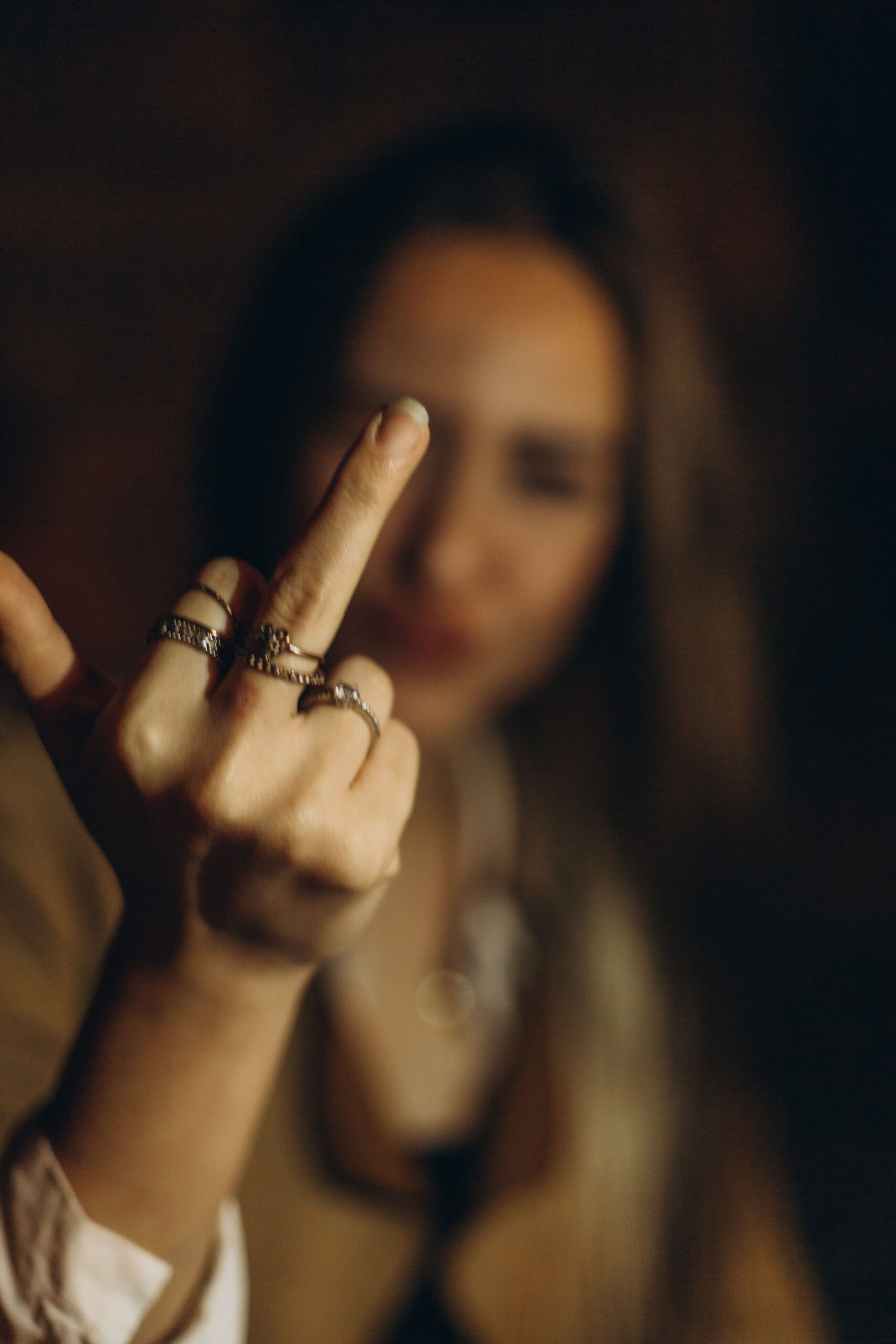 Blurred portrait with a hand in sharp focus raising a middle finger gesture.