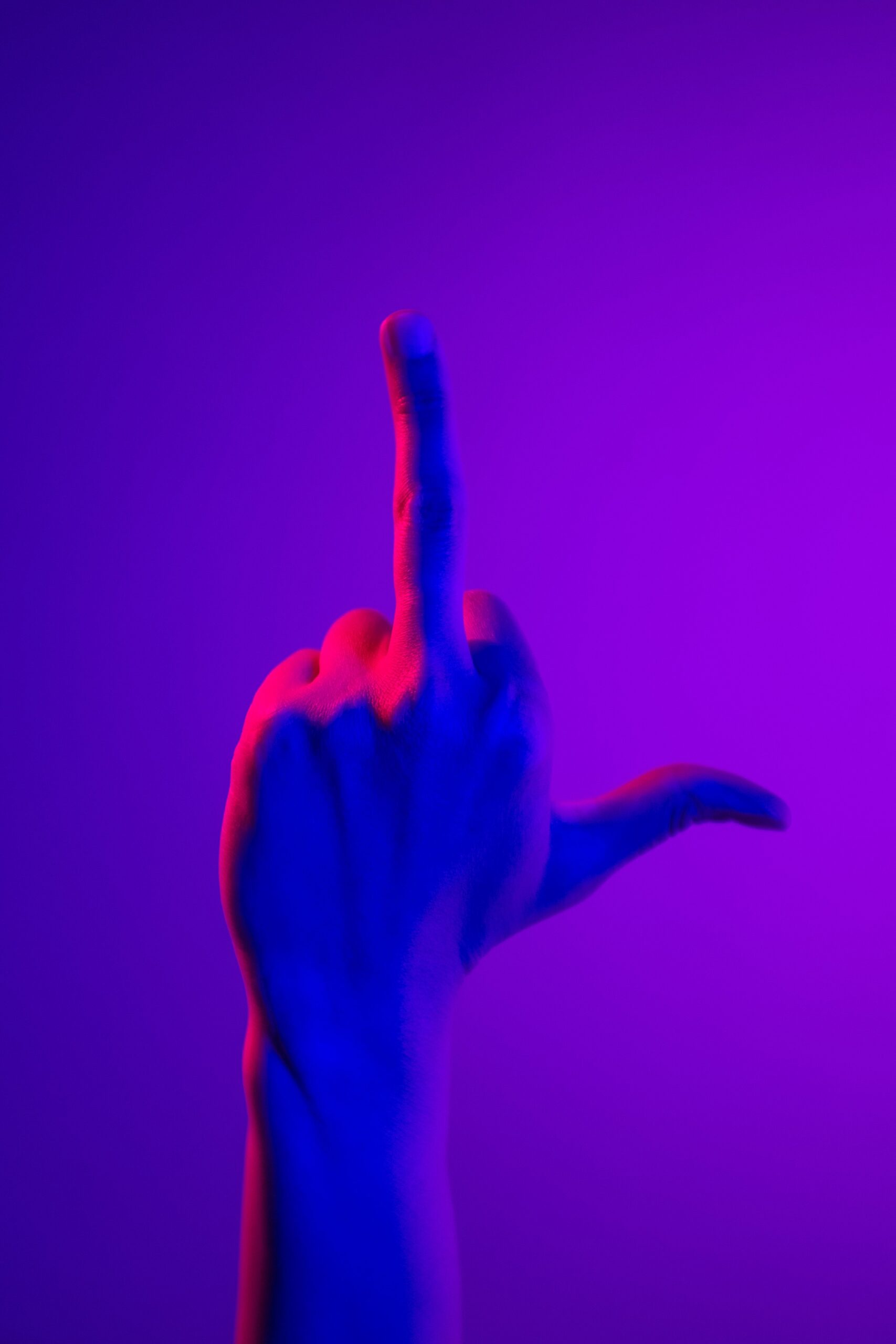 Palm-facing hand with only the middle finger raised, photographed in colored studio light.